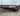 Red Tracker Pro V-175 fishing boat with Mercury motor on trailer, labeled OR 186 AFT, parked on lot under cloudy sky
